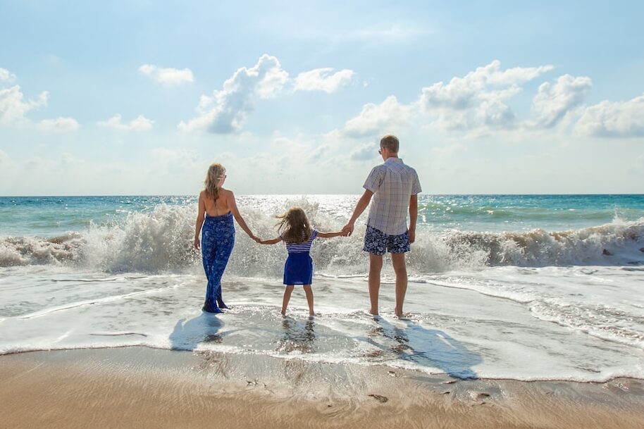 man, woman and child holding hands on seashore